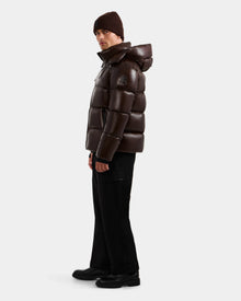 Wearing the Rudsak DANIEL S - M124508 Espresso men's shiny dark brown hooded down puffer, black pants and shoes, and a brown knit beanie, a person stands slightly turned against a plain white background.