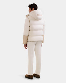 A man stands facing away, wearing the Rudsak DAVID - M125508 Vanilla men’s shearling puffer jacket with a hood, light pants, and dark brown shoes against a plain white background.