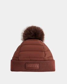 The Rudsak GALA - 8424514 Rust is a women's brown quilted down puffer hat with a large removable faux fur pom pom and folded brim featuring a rectangular RUDSAK patch.