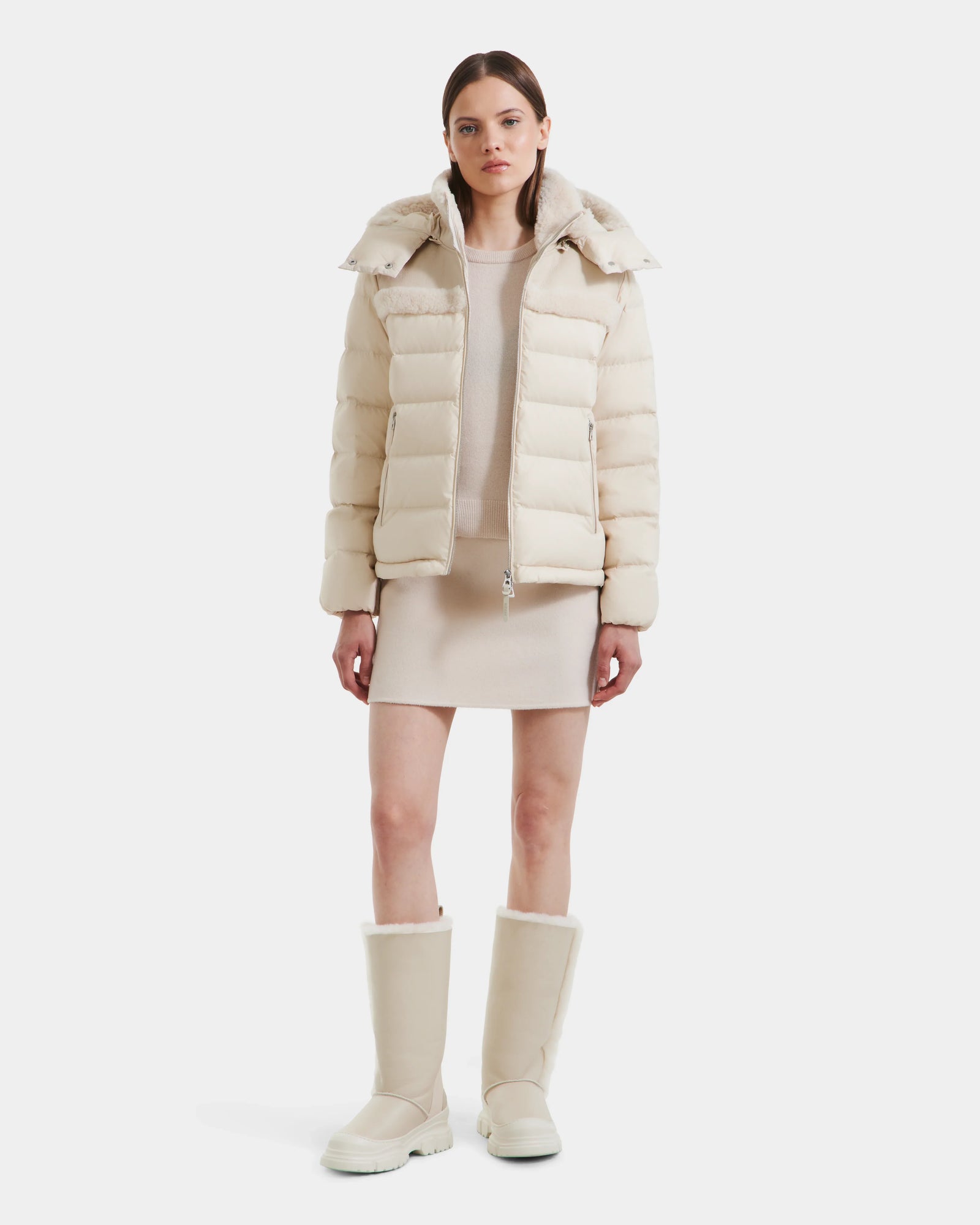 A woman faces forward in a modern look, wearing the Rudsak SANDRA - 8125612 Vanilla women’s shearling puffer jacket with a matching short dress and knee-high boots. She has straight brown hair and a neutral expression against a white background.