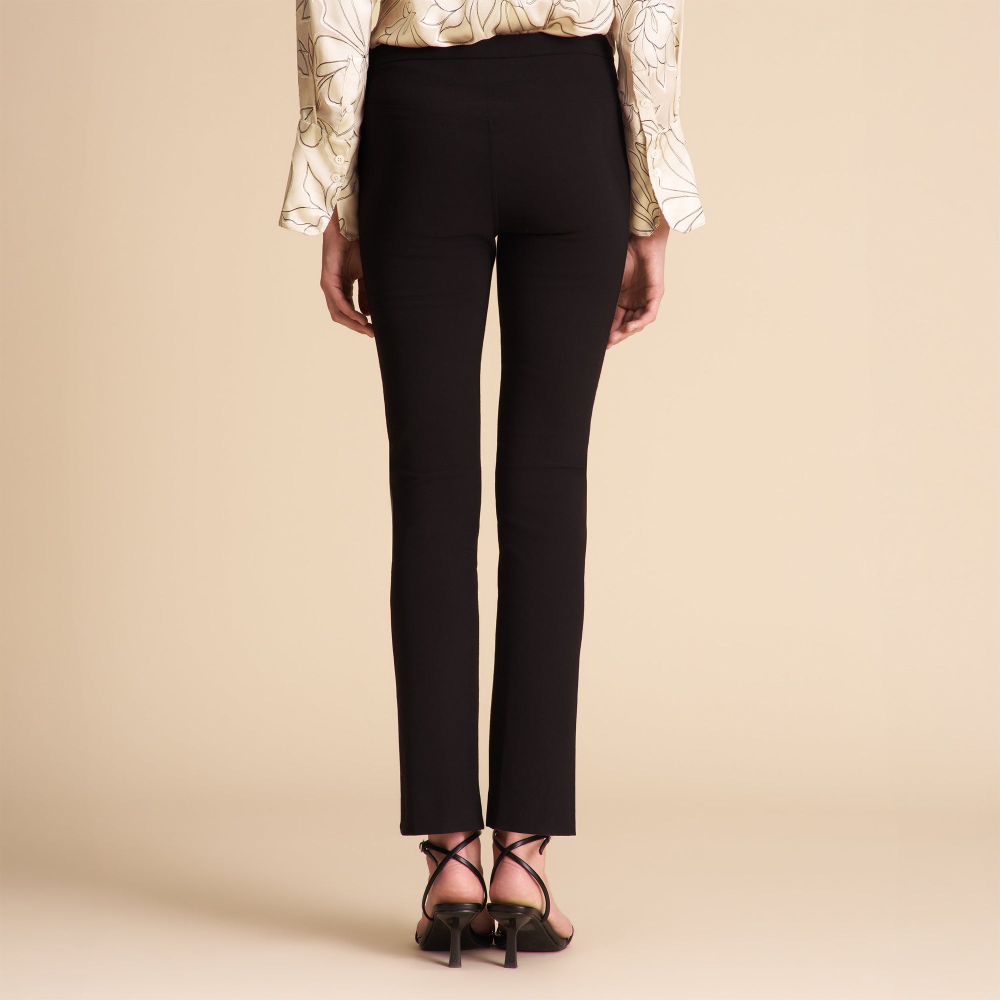 Person wearing black pants and a patterned top on a beige background
