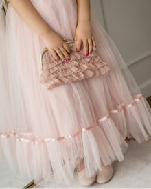 Girl holding dusty pink organza ruffle handbag against matching dress, featuring tiered ruffle detailing and gold metal frame