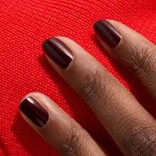 Three neatly manicured short nails in Manucurist's Hollyhock, a deep red polish, rest against vibrant red fabric, complementing a rich skin tone.