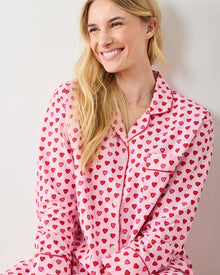 Model wearing the pink heart-print long pajama set, with a collared button-front top, chest pocket, and red piping