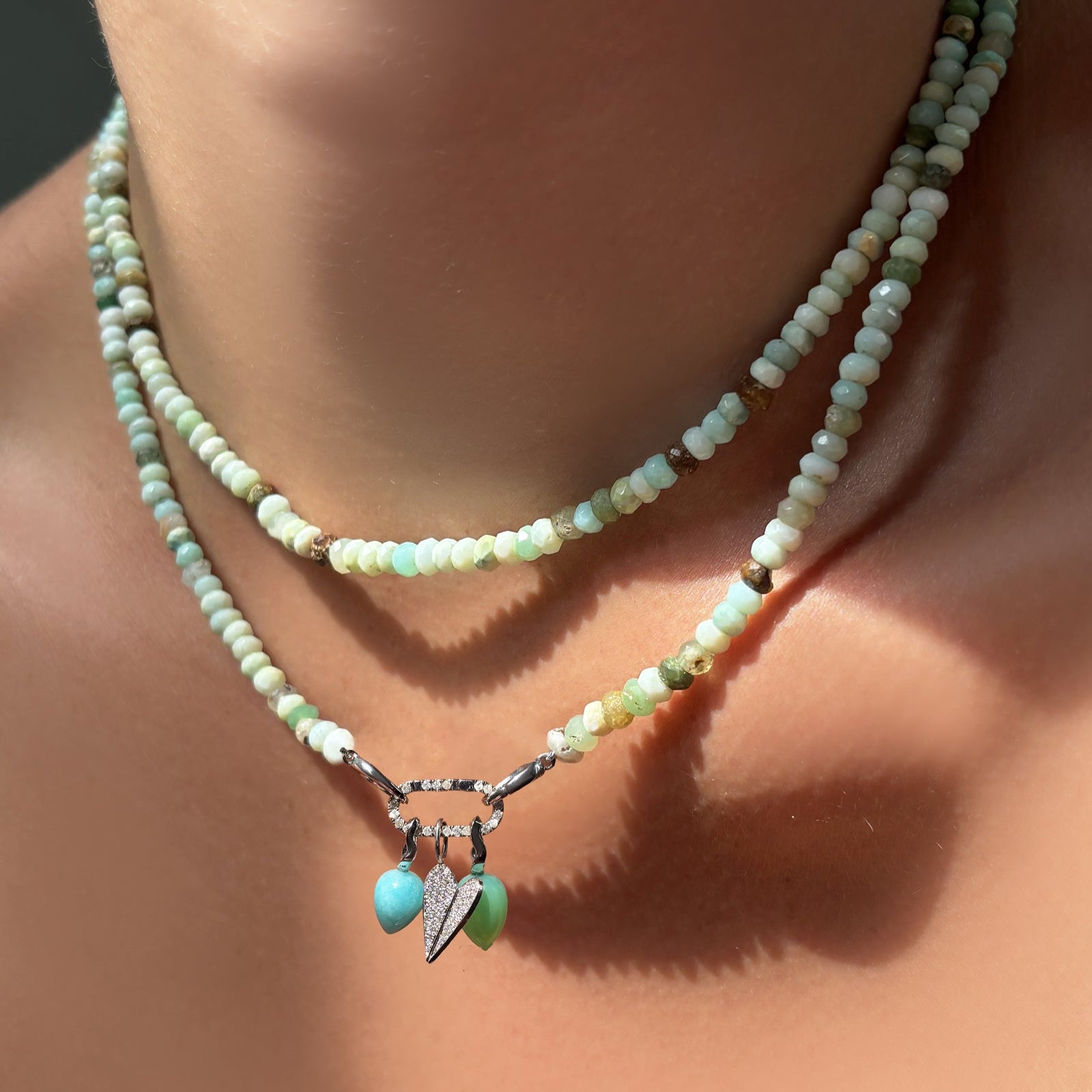 Peruvian green faceted opal necklaces layered on the neck with a medium pave face charm lock with chrysoprase and amazonite drop charms and a full pavé folded heart charm.