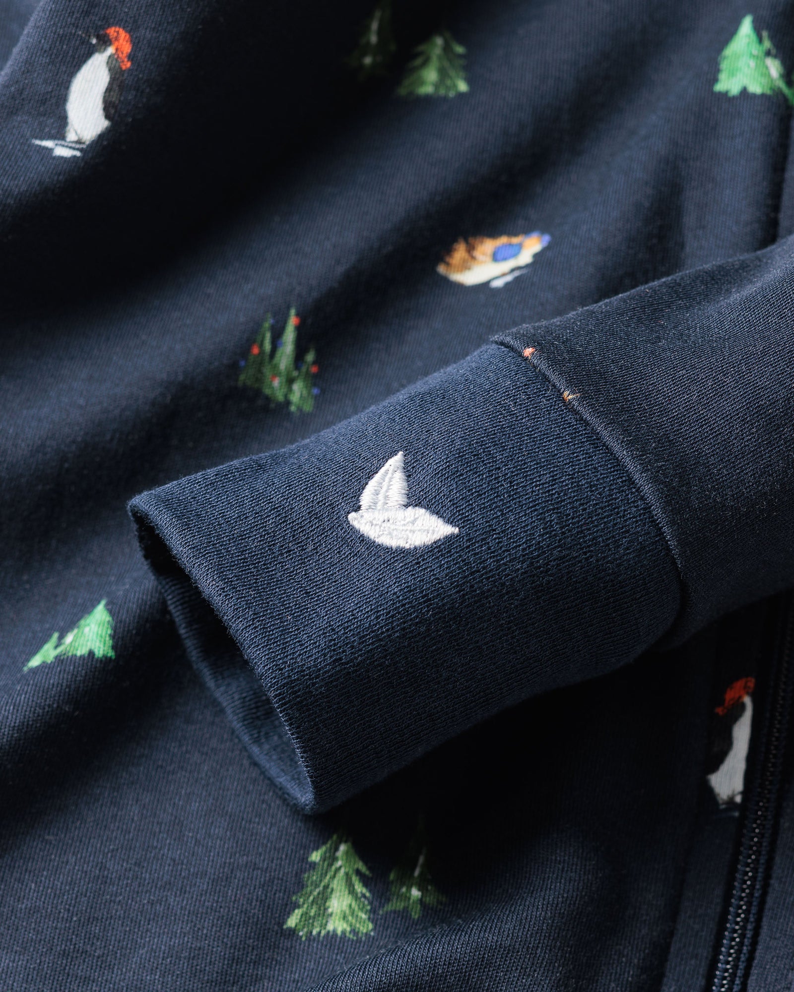 Close-up of Petite Plumes Babys Pima Romper in Arctic Antics, featuring a breathable dark blue fabric with embroidered small trees and birds, including a white bird on the cuff. Its soft texture and vibrant colors add whimsy to the design.