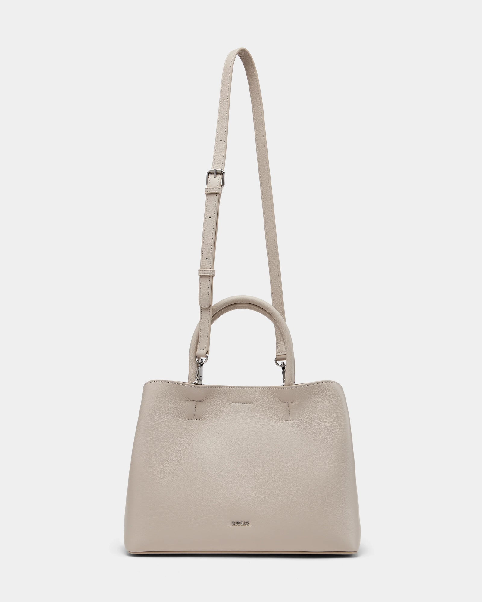 The Rudsak CATIRA S - 8325006 Vanilla women’s tote bag features beige pebble leather, a minimalist design, two short handles, a removable long strap, and a small metallic logo on the front.