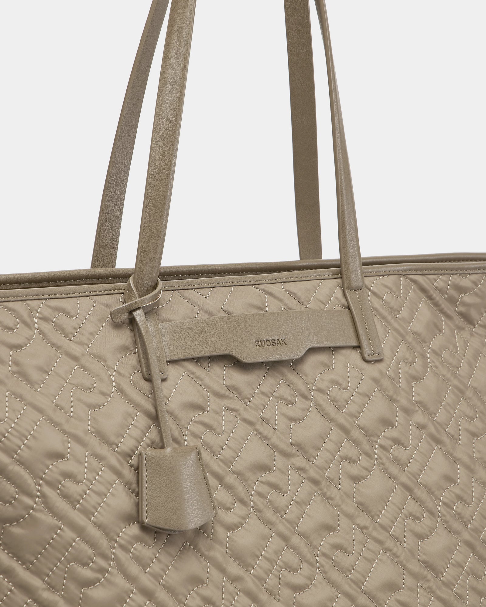 Close-up of the Rudsak LIVORNO - L325007 Almond tote bag featuring beige quilted monogram design, matching handles, geometric stitching, and a small attached leather tag.