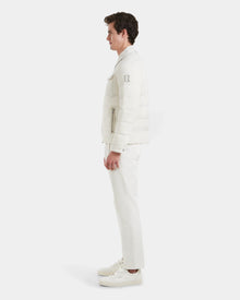 A man stands in profile against a white background, wearing the Rudsak ORNO - 6124601 Vanilla mens down quilted jacket with RDS-certified down, paired with white pants and sneakers.
