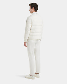 A man faces away, dressed in all-white with Rudsaks ORNO - 6124601 Vanilla mens down quilted jacket, pants, and sneakers, standing against a plain white background.
