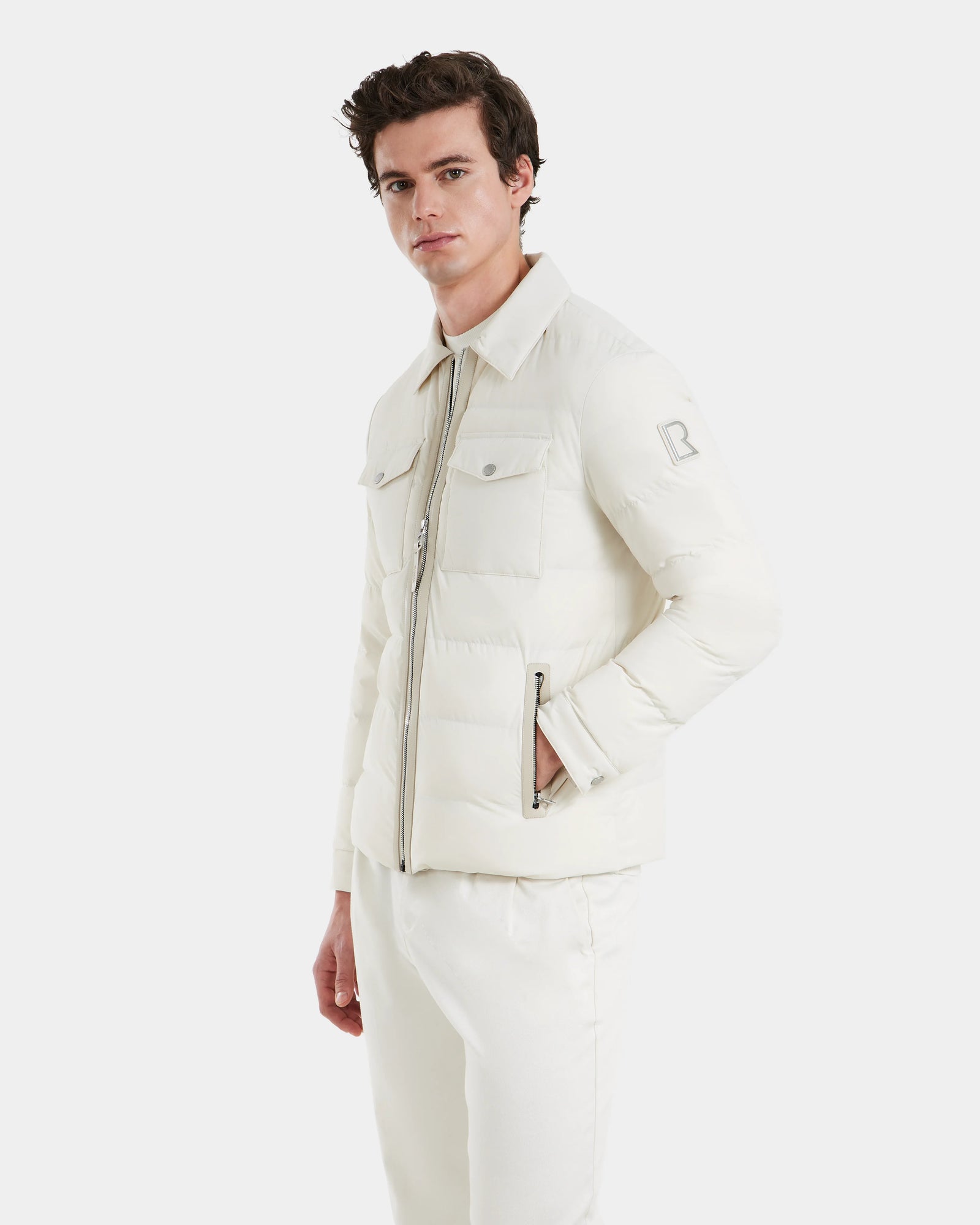 A young man wearing the Rudsak ORNO - 6124601 Vanilla mens down quilted shirt jacket with vegan leather trims and matching white pants stands against a plain white background, looking at the camera with a neutral expression.