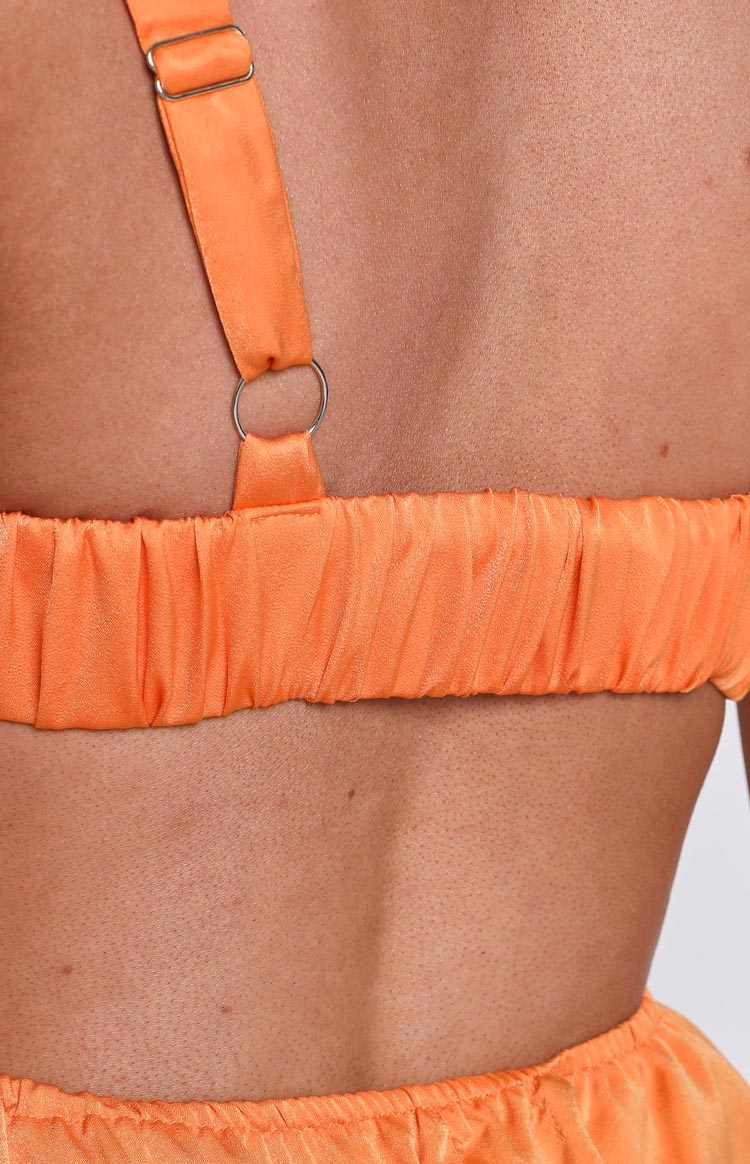 Close-up of the back of an orange mini dress showing the shirred elasticated band and adjustable strap with a silver O-ring