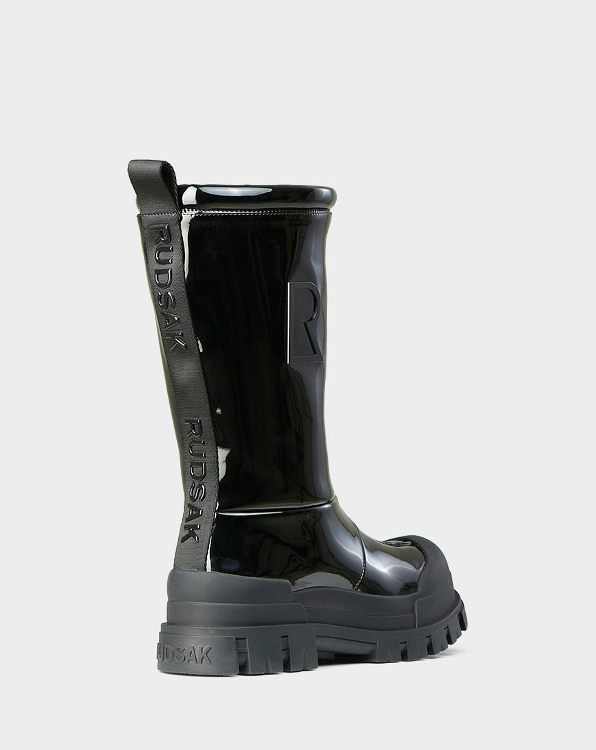The KRISTAL HI - 8222510 BLACK by Rudsak is a shiny black high-gloss winter boot with chunky grip soles, embossed Rudsak branding on the pull tab and heel, and a large R on the side, shown from the back and side against a light background.