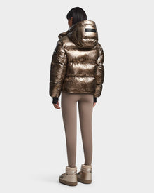 A person stands facing away, wearing the Rudsak MAVE S - 8123563 Metallic Ivory Camo women’s down puffer jacket against a plain white background.