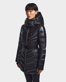 A woman wears the Rudsak MALAYA - L123510 Black down puffer jacket with herringbone quilting, high collar, hood, and belted waist, standing against a plain light background.