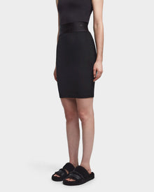A person wearing the CHEYNA - 8523514 Black faux suede pencil skirt by Rudsak, a black sleeveless top, and black fuzzy slide sandals stands against a plain white background.