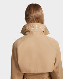 A person with straight, light brown hair is shown from behind wearing the Rudsak MIRELLE - 8124055 Khaki womens trench coat with a tailored silhouette and RUDSAK EST. 1994 embroidered on its turned-up collar.