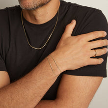 Model. Man wearing gold jewelry including a necklace, bracelet, and ring on a neutral background