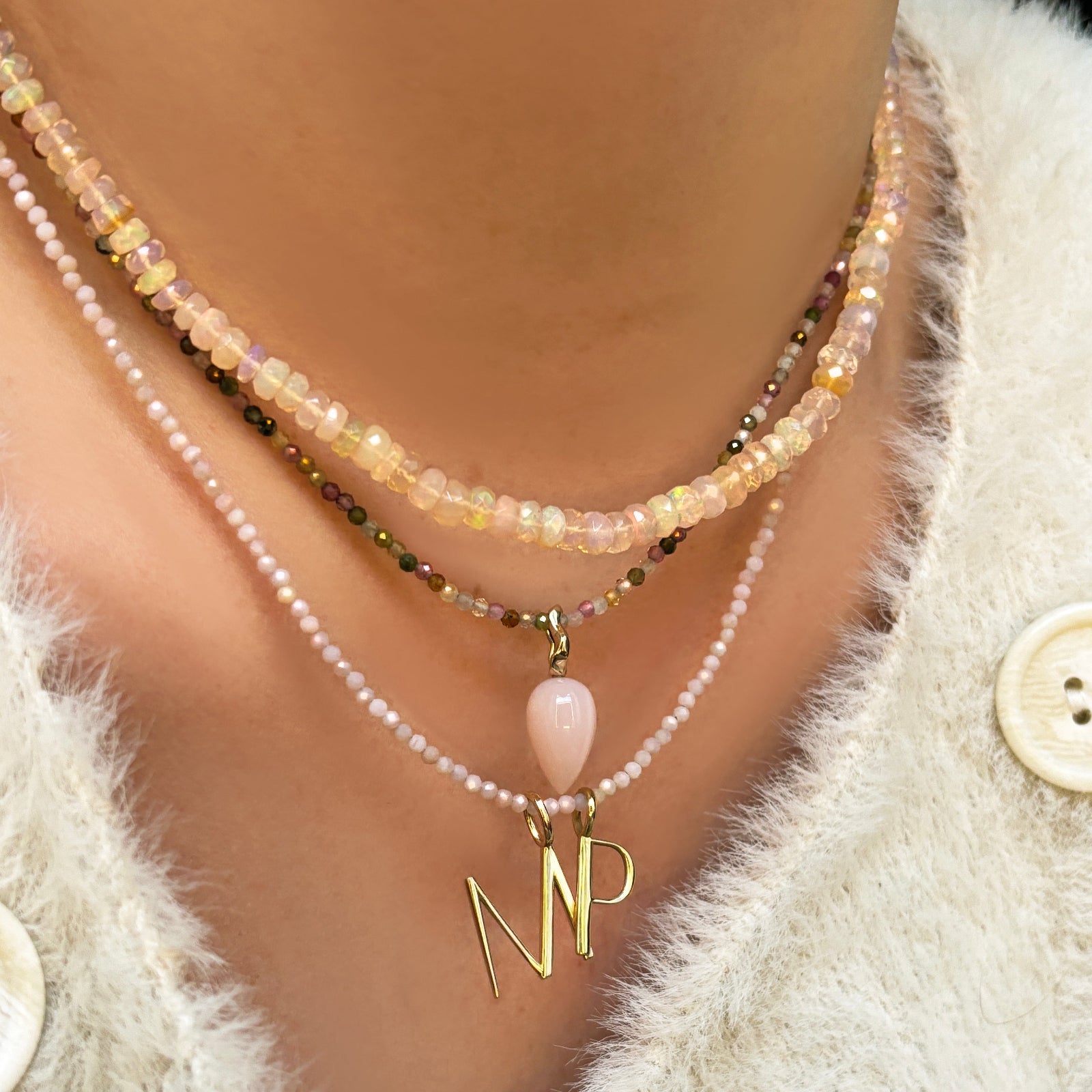 Blush faceted opal necklace with tourmaline and pink opal slim gemstone necklaces with pink opal drop charm and letter charms on the neck.