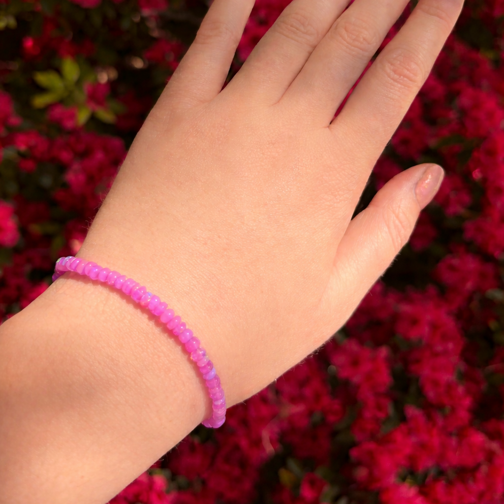 Hand wearing a pink beaded bracelet against a red floral background