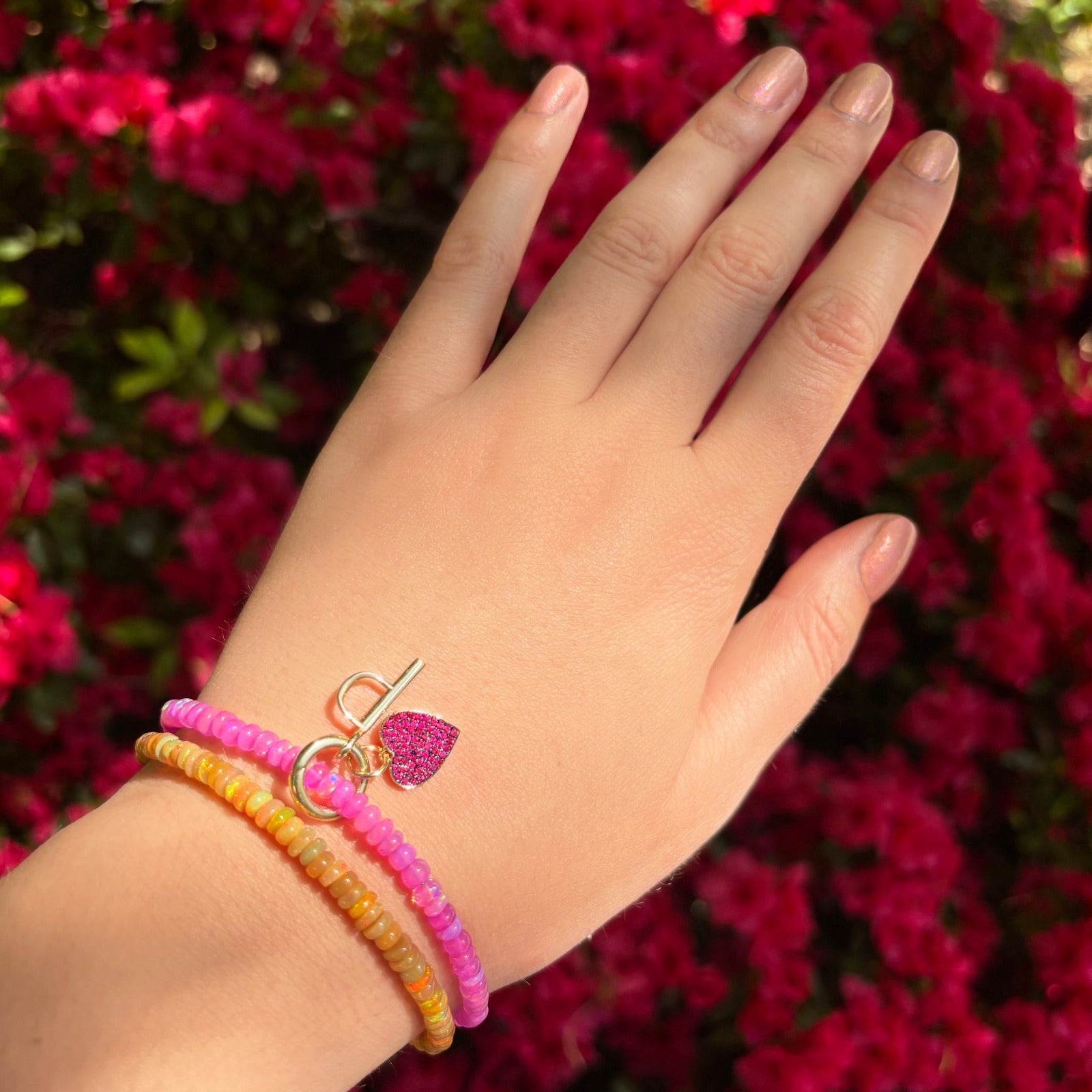 Shimmering beaded bracelet made of faceted opals in shades of bright pink on a gold linking lobster clasp. Styled on a wrist with a medium pave heart and P letter charm. 