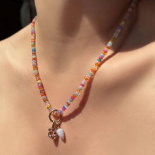 High-biscus opal necklace with beaded round charm lock, molten knot charm with amethyst, and blue lace agate drop charm hanging from the neck.