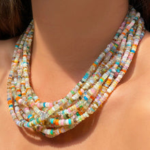 Shimmering beaded necklace made of smooth opal rondels in shades of tan, teal, orange and pink on a gold linking ovals clasp. Styled on a neck layered together.