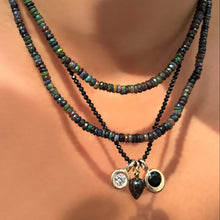 night sky faceted opal necklace layered over black spinel slim gemstone necklace holding a quill bezel charm, rutilated quartz drop charm, and black onyx molten solitaire charm on a model's neck.
