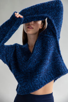 Model partially covering her face while wearing a Sky Navy sweater made from 89% superfine alpaca and 11% nylon, highlighting its cozy texture.